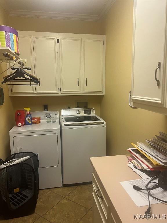 clothes washing area featuring crown molding, cabinets, washer and clothes dryer, and dark tile patterned floors