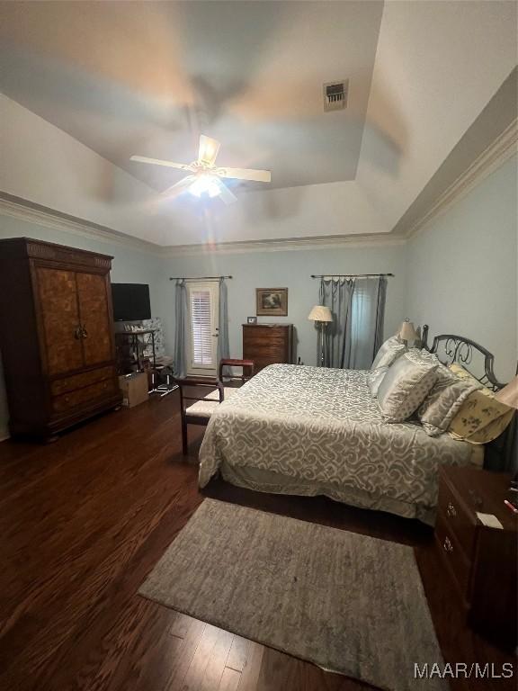 bedroom with a tray ceiling, crown molding, dark hardwood / wood-style floors, and ceiling fan