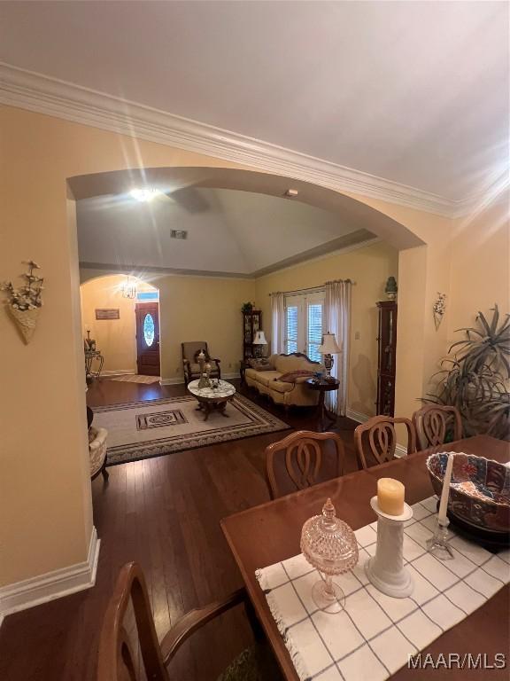 dining space with wood-type flooring, ornamental molding, and vaulted ceiling