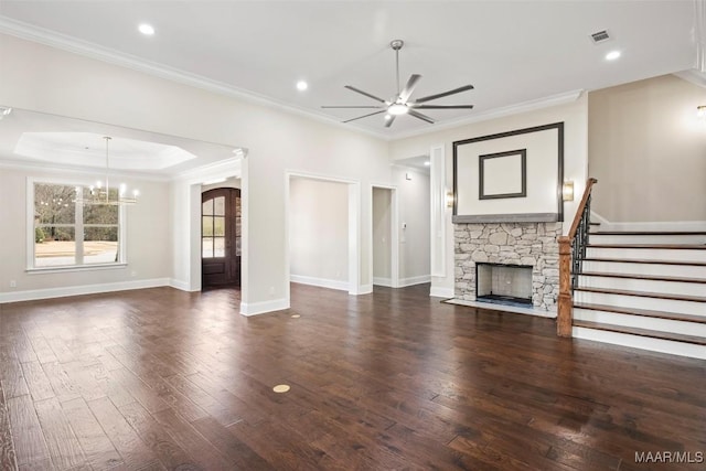 unfurnished living room featuring a stone fireplace, ceiling fan with notable chandelier, a raised ceiling, crown molding, and dark wood-type flooring