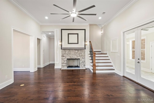 unfurnished living room featuring crown molding, dark wood-type flooring, ceiling fan, a stone fireplace, and french doors