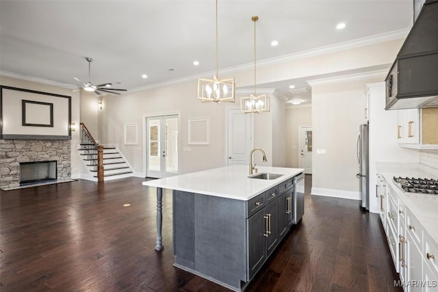 kitchen with pendant lighting, white cabinetry, sink, stainless steel appliances, and a center island with sink