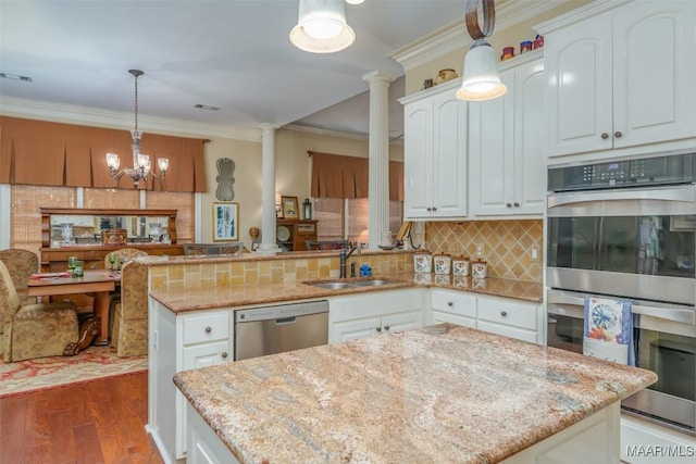 kitchen with sink, appliances with stainless steel finishes, white cabinetry, hanging light fixtures, and light stone counters