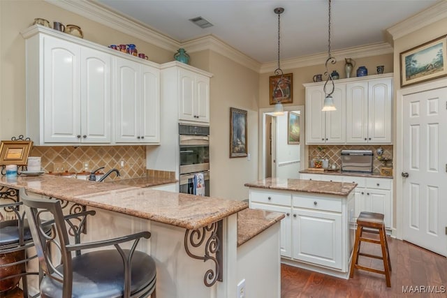 kitchen featuring pendant lighting, double oven, light stone counters, a kitchen bar, and kitchen peninsula