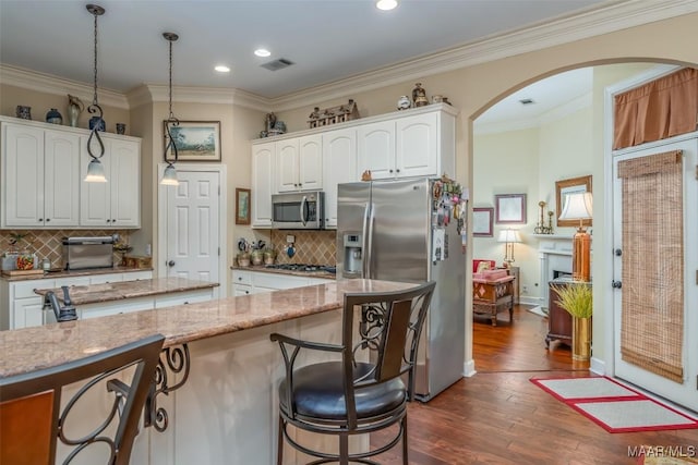 kitchen with stainless steel appliances, white cabinetry, light stone countertops, and hanging light fixtures