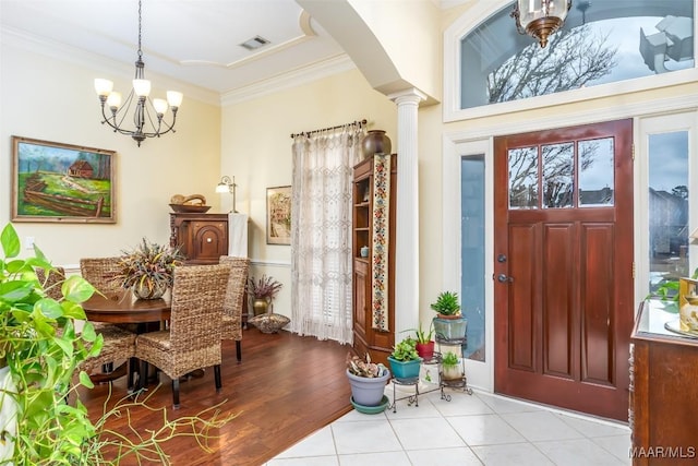 foyer featuring ornate columns, ornamental molding, a notable chandelier, and light hardwood / wood-style flooring