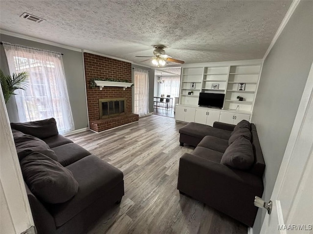 living room featuring wood-type flooring, ornamental molding, ceiling fan, a brick fireplace, and a textured ceiling