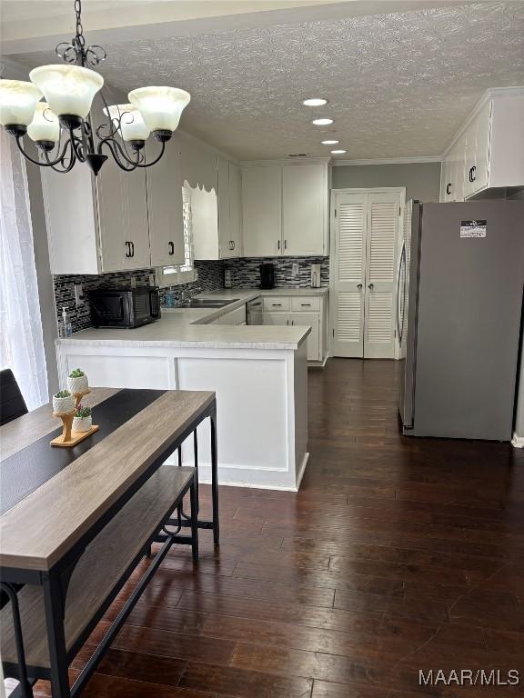 kitchen featuring white cabinetry, stainless steel fridge, dark hardwood / wood-style flooring, hanging light fixtures, and kitchen peninsula