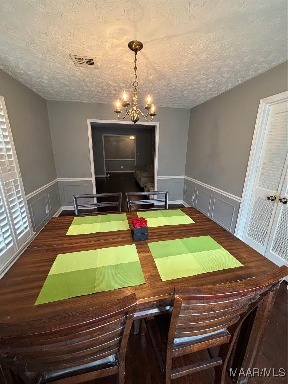 dining room featuring a textured ceiling, a wainscoted wall, visible vents, a decorative wall, and a notable chandelier