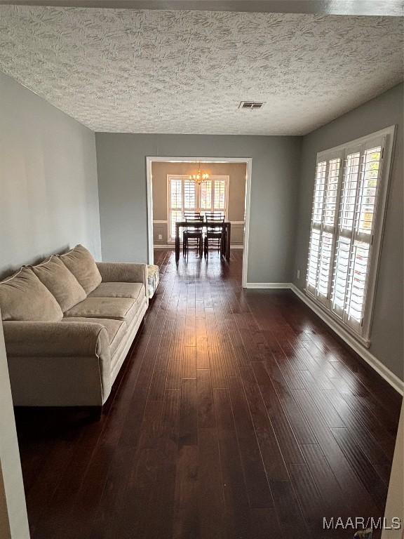 living room featuring a textured ceiling, visible vents, baseboards, dark wood-type flooring, and an inviting chandelier
