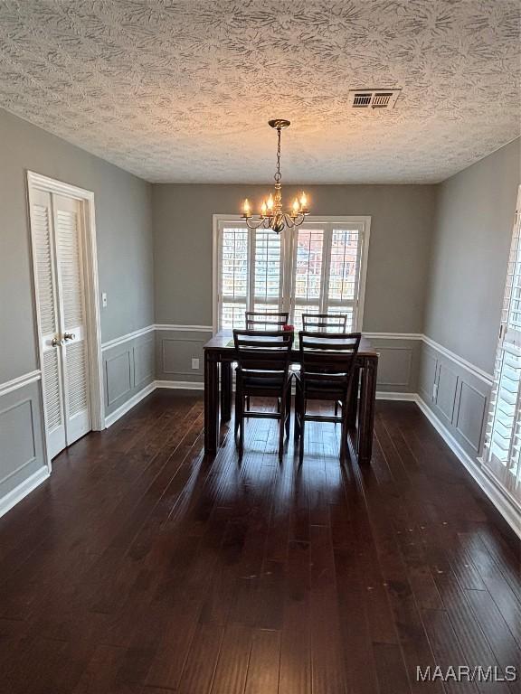 dining space featuring dark wood finished floors, a notable chandelier, a textured ceiling, and visible vents