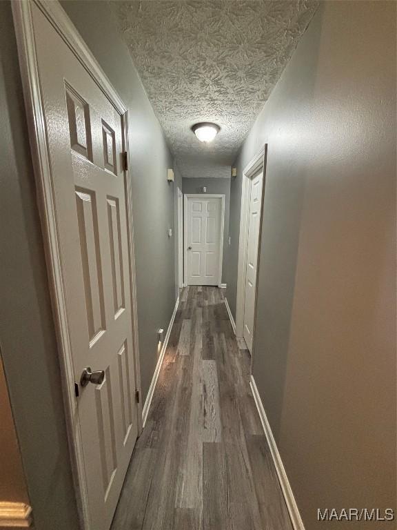 hallway with dark wood finished floors, baseboards, and a textured ceiling