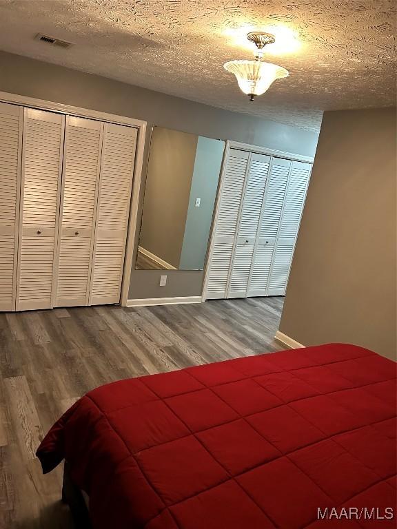 bedroom featuring baseboards, visible vents, wood finished floors, and a textured ceiling