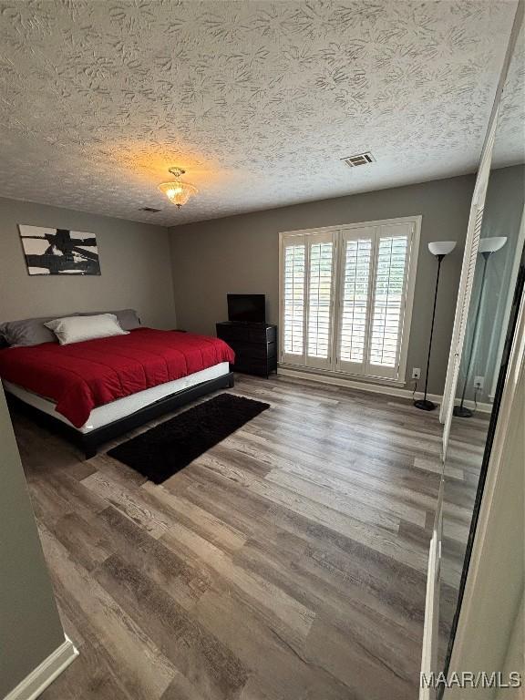 bedroom with visible vents, a textured ceiling, baseboards, and wood finished floors