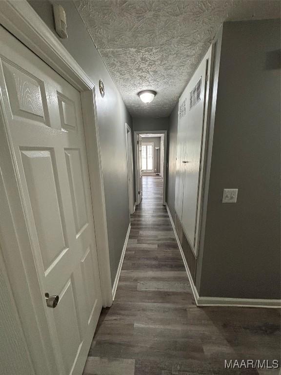 hallway featuring dark wood-style flooring, visible vents, baseboards, and a textured ceiling