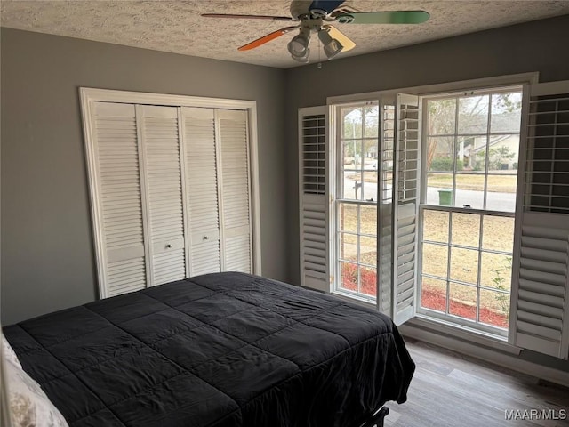 bedroom with a closet, a textured ceiling, ceiling fan, and light wood-type flooring