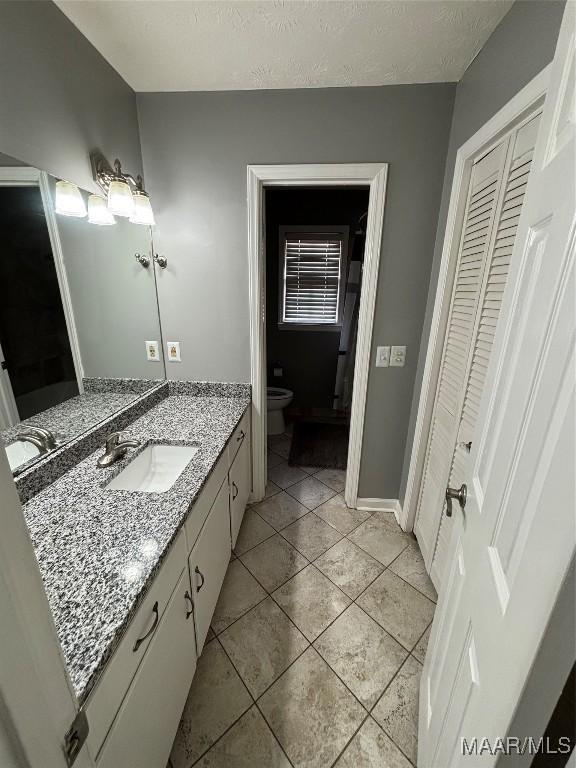 bathroom with vanity, toilet, a textured ceiling, tile patterned floors, and a closet