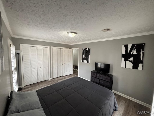 bedroom with ornamental molding, dark hardwood / wood-style floors, a textured ceiling, and two closets