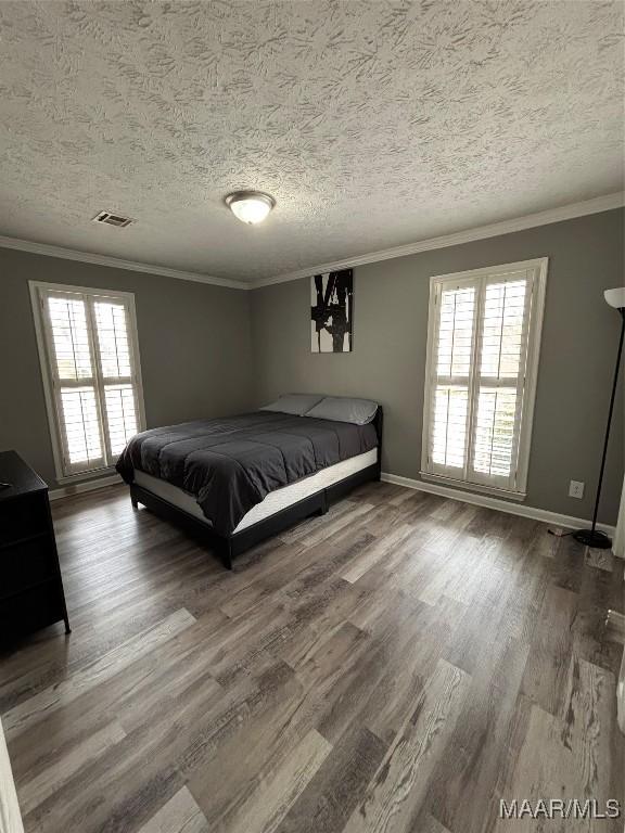 bedroom featuring hardwood / wood-style flooring, ornamental molding, a textured ceiling, and multiple windows