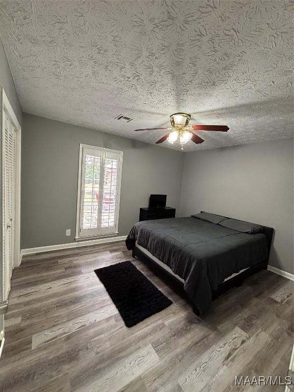 bedroom featuring wood finished floors, a textured ceiling, baseboards, visible vents, and ceiling fan