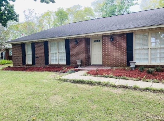 ranch-style home featuring brick siding, a shingled roof, and a front yard