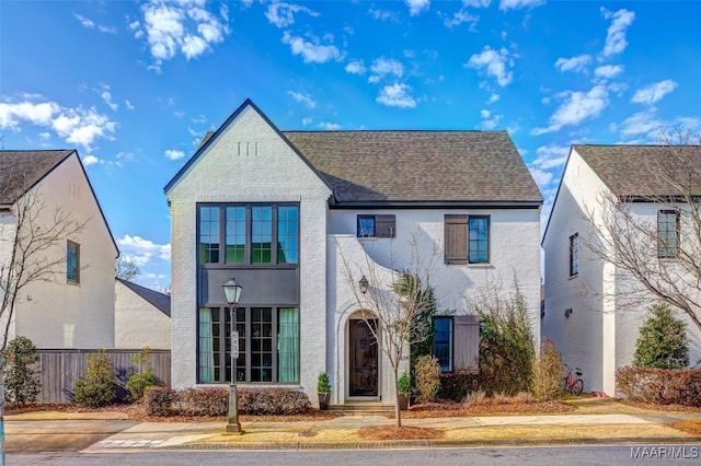 view of front of house featuring a shingled roof, fence, and brick siding