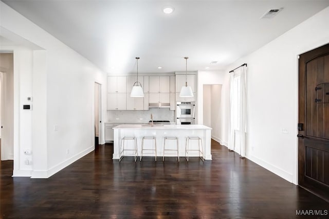 kitchen with a center island with sink, a breakfast bar, light countertops, double oven, and pendant lighting