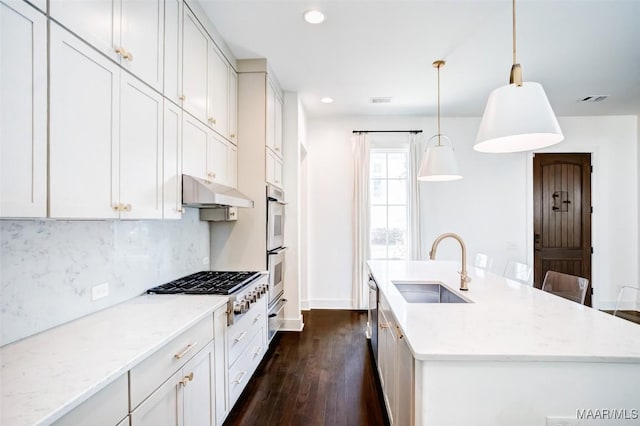 kitchen featuring light stone counters, pendant lighting, a kitchen island with sink, white cabinets, and under cabinet range hood