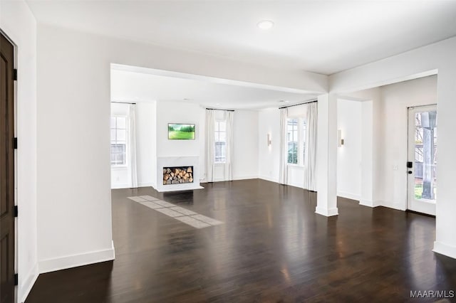 unfurnished living room featuring plenty of natural light, a premium fireplace, baseboards, and dark wood finished floors