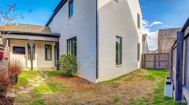 view of property exterior with fence, a lawn, and brick siding