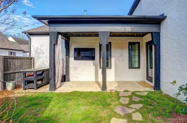 rear view of property featuring a yard, brick siding, a patio, and fence