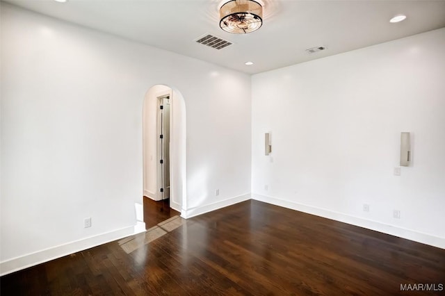 spare room featuring arched walkways, recessed lighting, dark wood-type flooring, visible vents, and baseboards