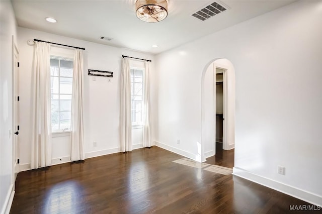 spare room featuring baseboards, visible vents, arched walkways, and dark wood-style flooring