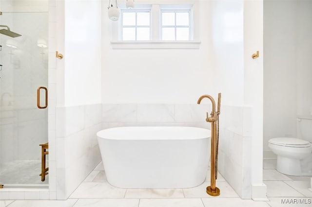 bathroom featuring a stall shower, a freestanding tub, wainscoting, and tile walls