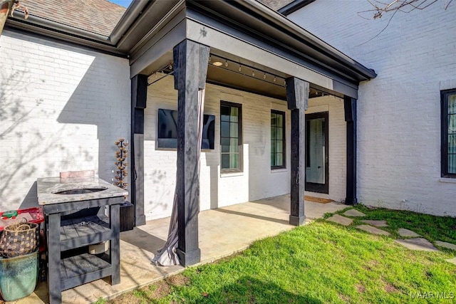 doorway to property featuring a patio area, brick siding, and a shingled roof