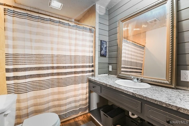 bathroom with wooden walls, sink, hardwood / wood-style flooring, toilet, and a textured ceiling