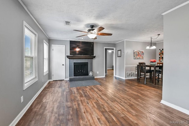 unfurnished living room with a fireplace, ornamental molding, a textured ceiling, dark hardwood / wood-style flooring, and ceiling fan with notable chandelier