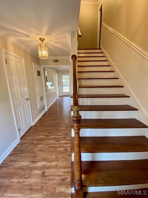 stairs with wood-type flooring and ornamental molding