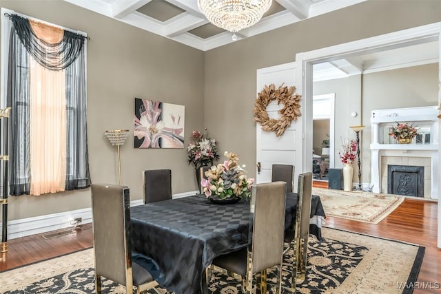 dining area featuring a tiled fireplace, hardwood / wood-style floors, coffered ceiling, and beamed ceiling