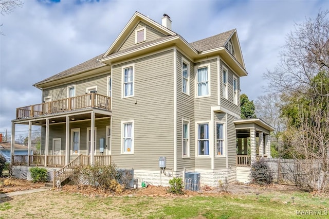 view of front facade with central AC unit, a front lawn, a balcony, and covered porch