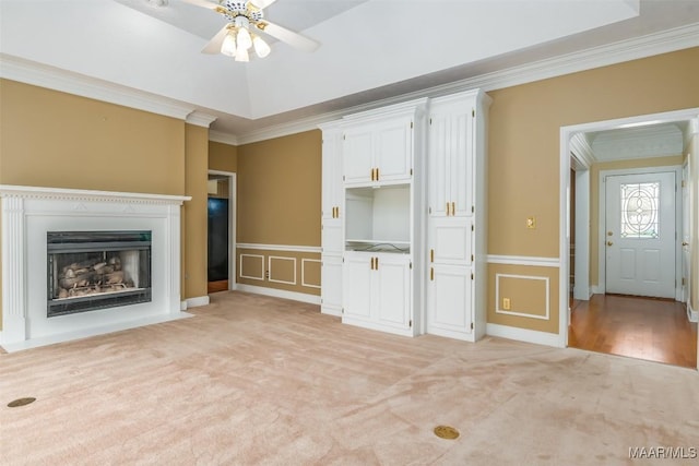 unfurnished living room with crown molding, ceiling fan, a tray ceiling, and light carpet