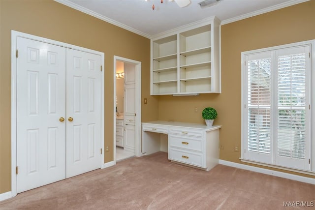 unfurnished office featuring ornamental molding, built in desk, and light colored carpet