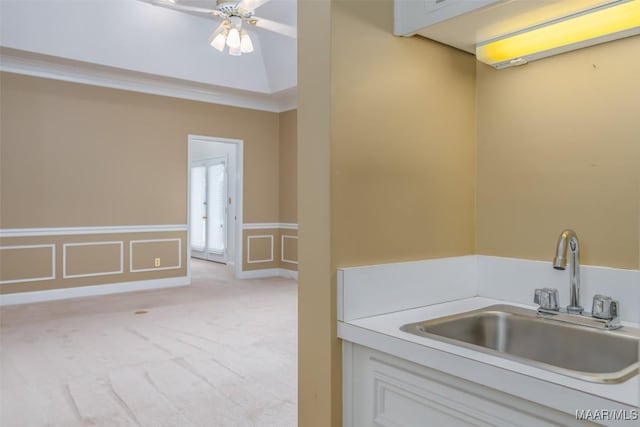 kitchen with sink, ceiling fan, ornamental molding, white cabinets, and light colored carpet