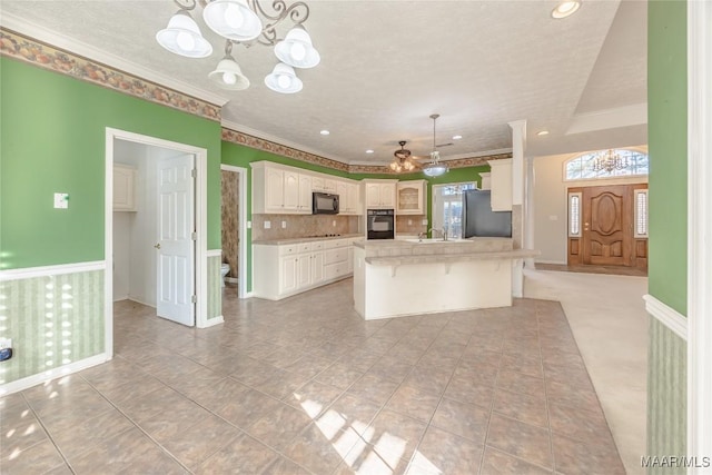 kitchen featuring an inviting chandelier, a center island, black appliances, white cabinets, and decorative light fixtures