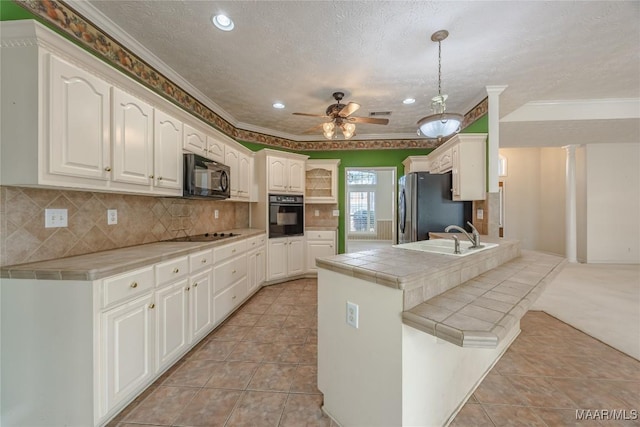 kitchen with decorative light fixtures, black appliances, sink, tile counters, and kitchen peninsula