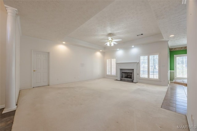 unfurnished living room with ornate columns, light colored carpet, ceiling fan, a raised ceiling, and a textured ceiling