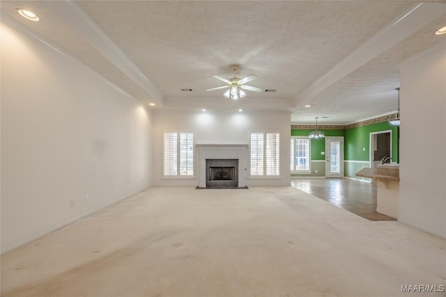 unfurnished living room featuring a premium fireplace, a tray ceiling, ornamental molding, a textured ceiling, and light colored carpet