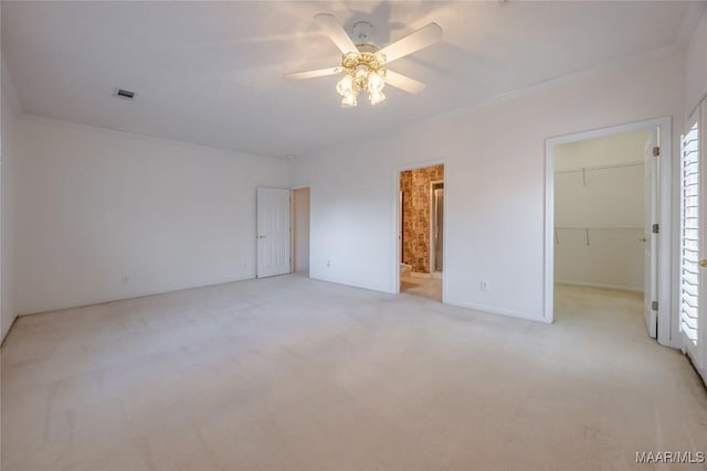 unfurnished bedroom with ceiling fan, ensuite bathroom, light carpet, a walk in closet, and a closet