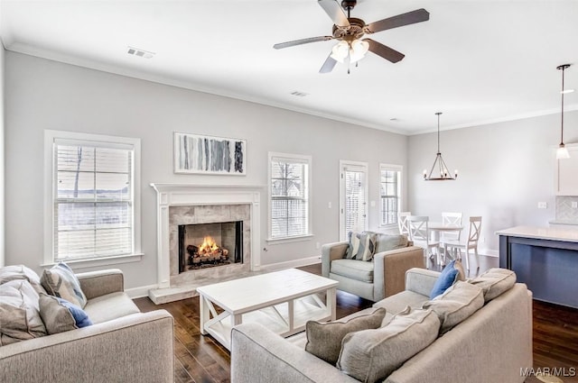 living room with a premium fireplace, ornamental molding, dark wood-type flooring, and ceiling fan with notable chandelier