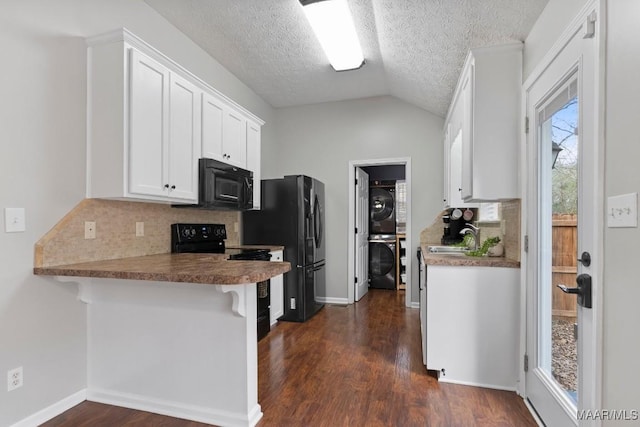 kitchen featuring stacked washer and clothes dryer, black appliances, a kitchen breakfast bar, kitchen peninsula, and white cabinets